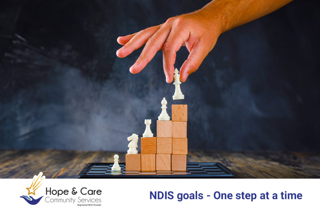 Image Description : Breaking Down the NDIS goals - The easier Way- stating a hand lifting up chess piece on a stage having steps showing "steps as goals" with different chess piece at each step.